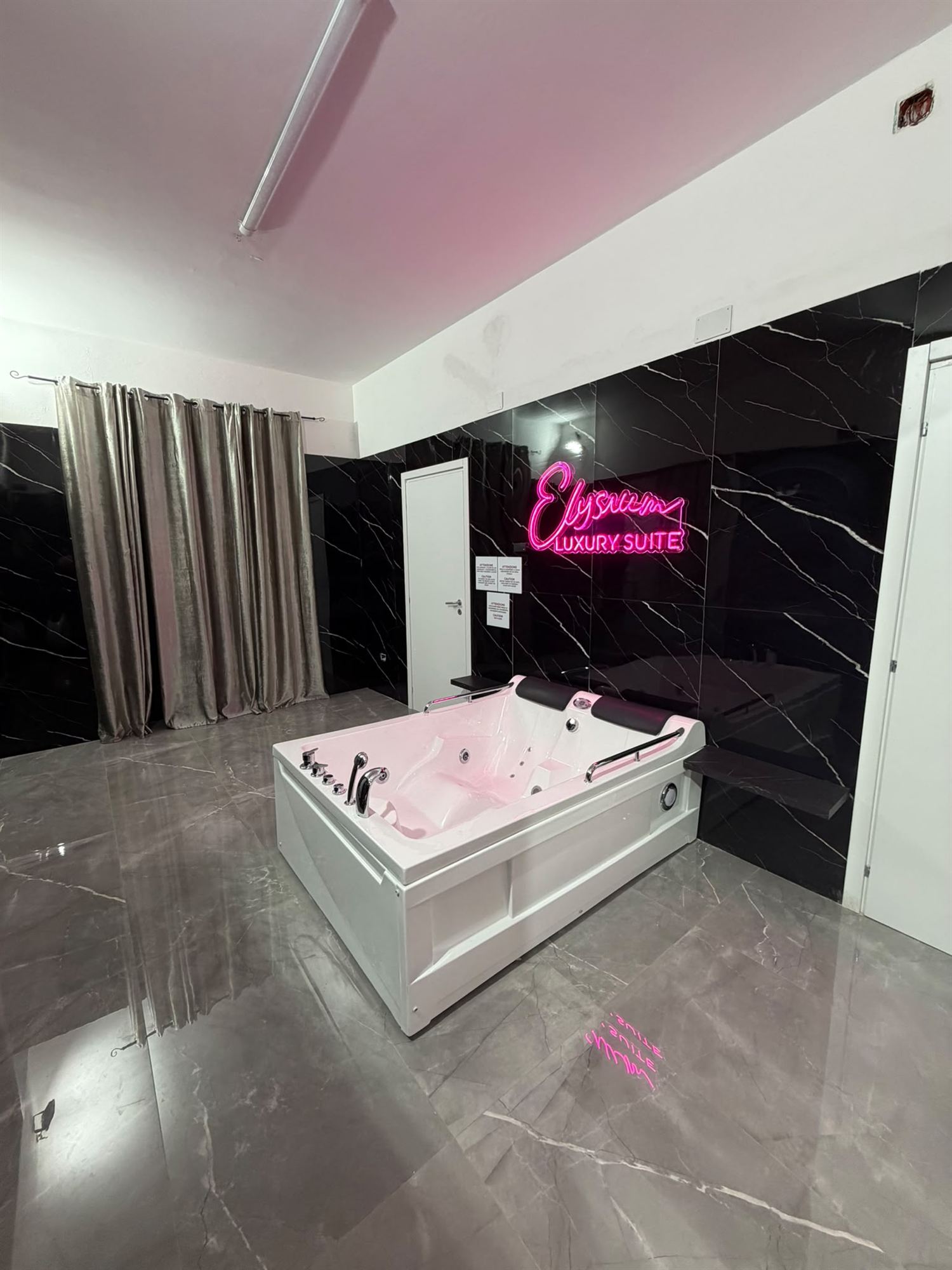 La suite Elysium con la vasca idromassaggio al centro e l'insegna neon sul marmo nero